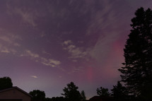 red  Aurora pillars, some clouds, and tree silhouettes