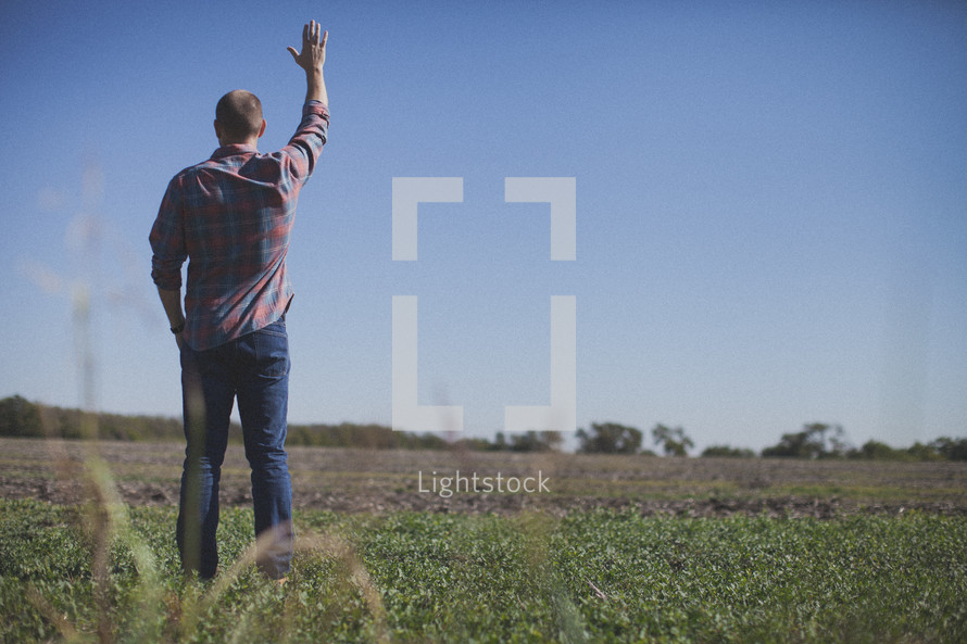 man standing in a field with raised hand