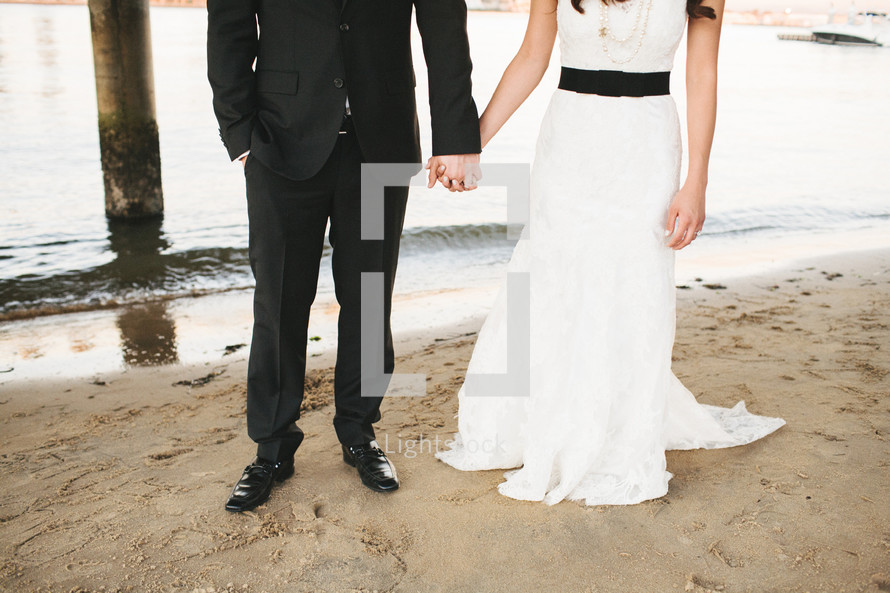 Bride and groom holding hands on beach.