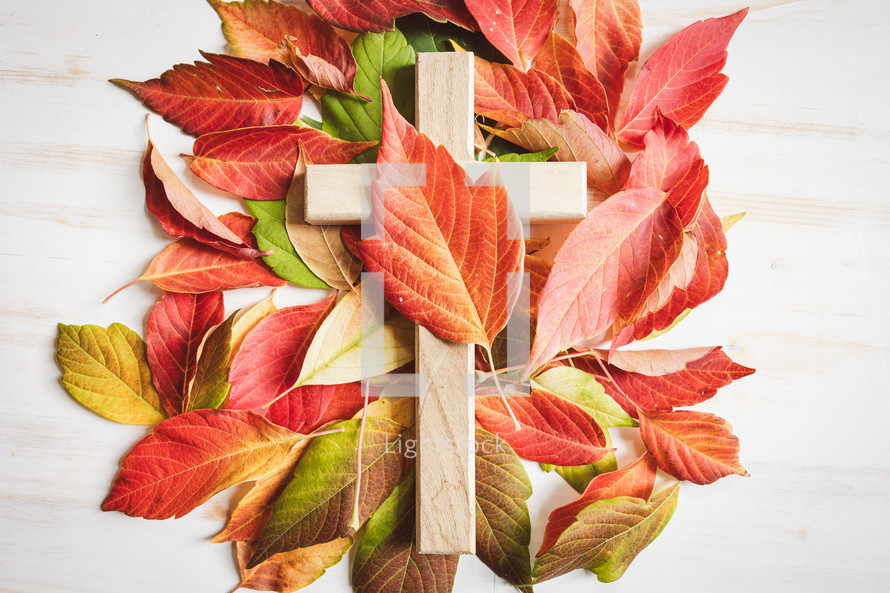 Wood cross with autumn leaves on a white wood background with copy space