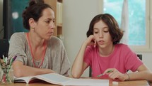 Mother helping her daughter to prepare homework at home