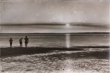 people standing on a shore at sunset 