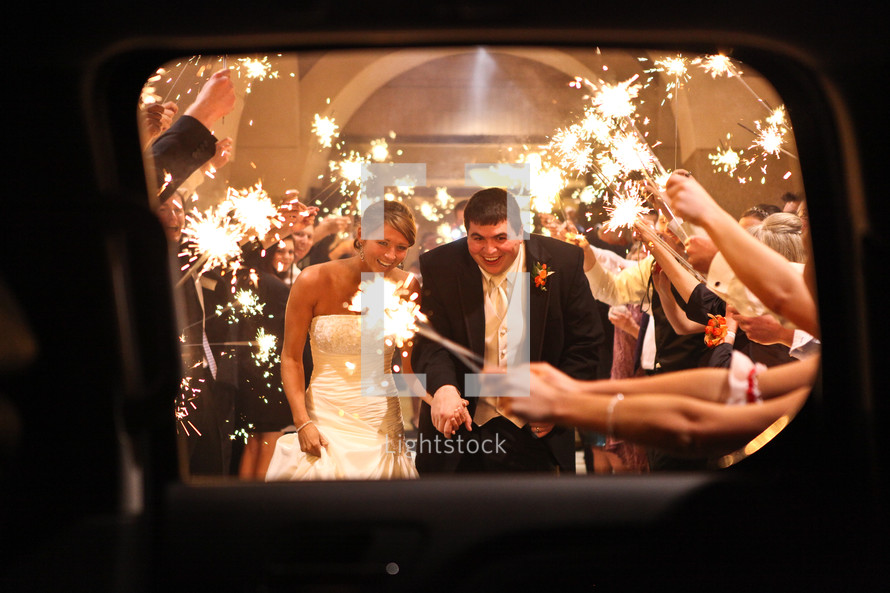 people holding sparklers over a bride and groom as the leave for their honeymoon