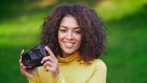 African Woman In Yellow Takes Pictures With DSLR Camera Over Green Background.