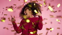 Happy woman dancing, having fun, rejoices over confetti rain in pink studio. 
