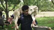 A happy middle eastern, Muslim man lovingly holds and carries a sheep on his shoulders in cinematic slow motion.