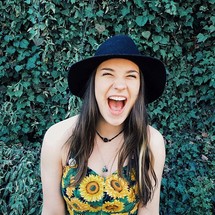 A laughing girl standing against a wall of ivy.