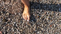 Top view of a woman's feet walking along a rocky beach shore.