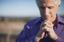 a man with praying hands outdoors 