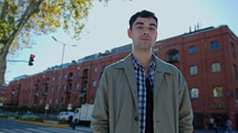 Young handsome man standing outdoors on the street and posing for the camera with a confident look and smile at daytime in the city. Medium shot, video portrait
