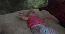 Infant girl laying on sheep skin bed overlooking forest - trendy kids