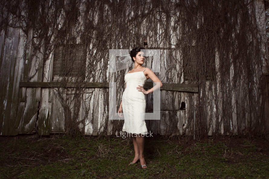 bride standing in front of an old barn covered in dead ivy
