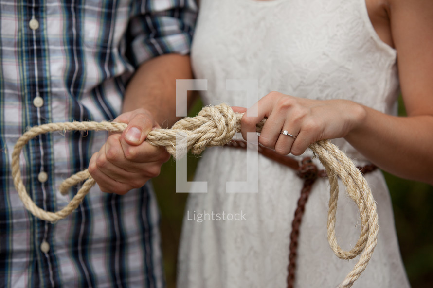 Couple tying a knot in a rope.