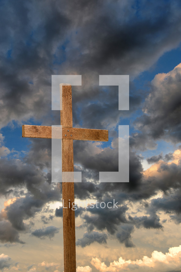 Wooden cross under storm clouds at sunset.