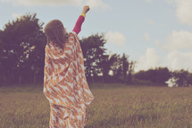a girl wrapped in a blanket standing in a field pointing up 