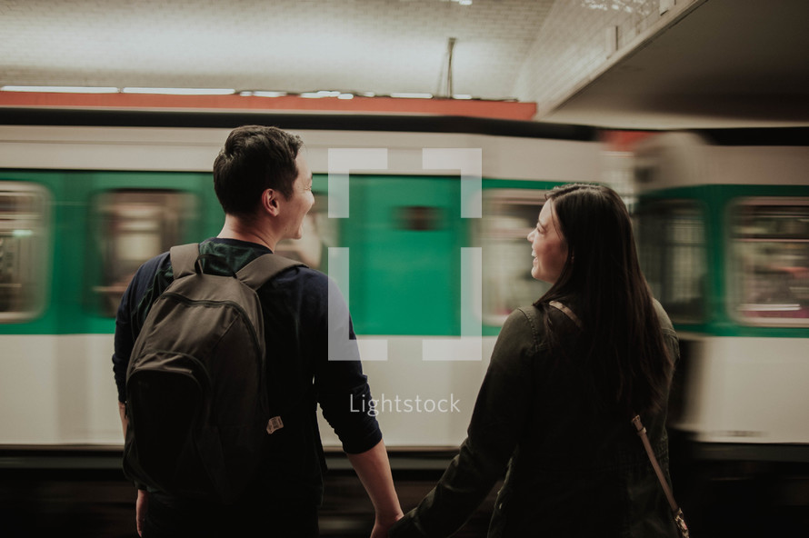 couple holding hands in front of a passing subway train 