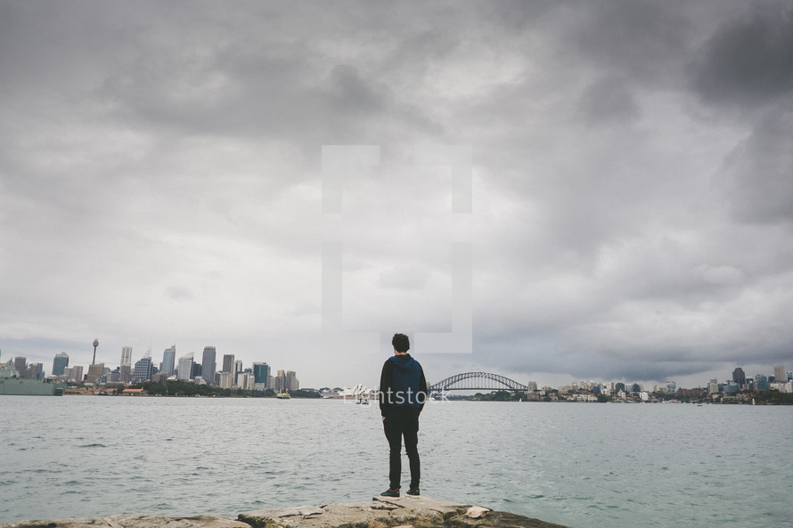 a man standing looking at a city across the river 