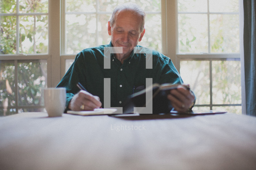 man reading a Bible and writing in a journal 