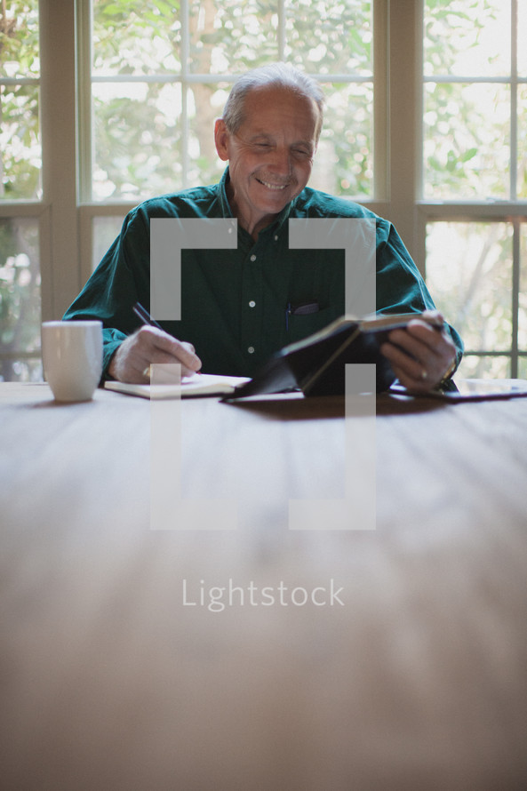 man reading a Bible and writing in a journal 