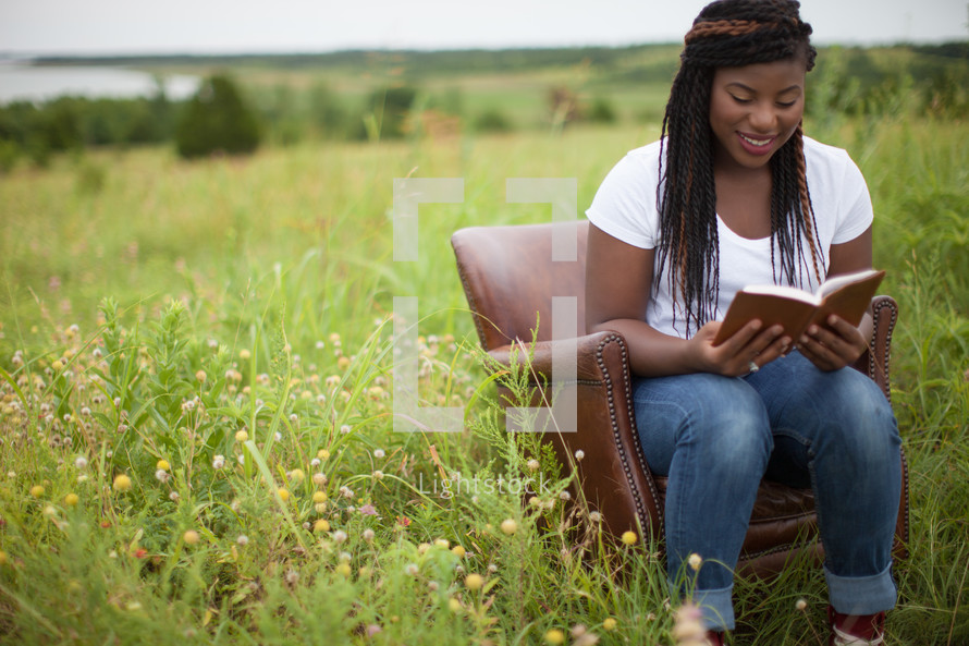 African-American woman sitting in a chair outdoors reading a Bible 