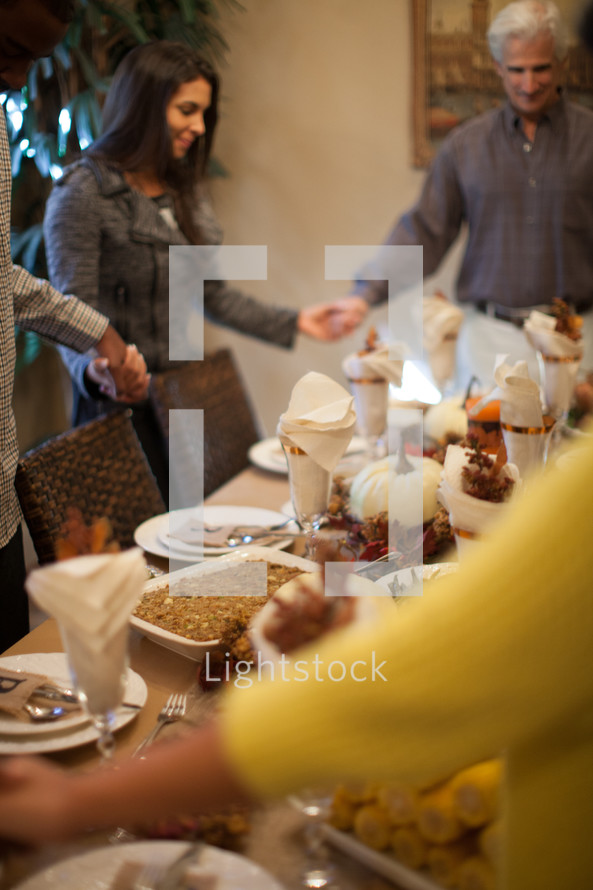 family holding hands in prayer around a Thanksgiving dinner table 