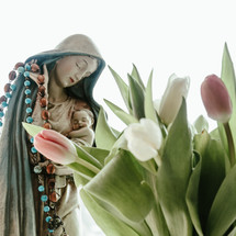 statue of Mary and Jesus holding a rosary and tulips 