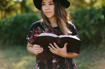teen girl in a hat holding a Bible outdoors 