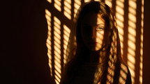 Portrait of beautiful girl in shadow of blinds on dark background