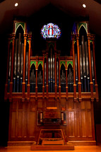 Old, ornate pipe organ with a stain-glass window above it