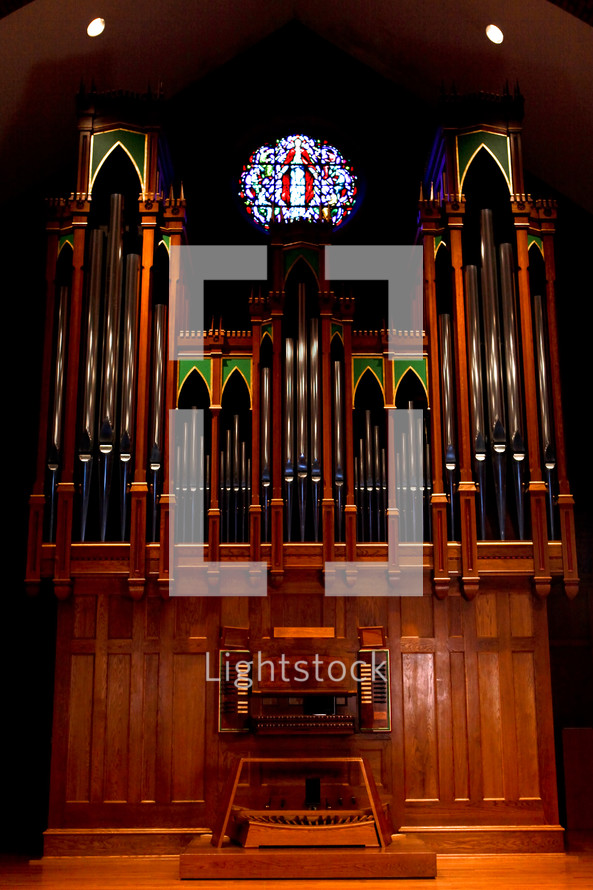 Old, ornate pipe organ with a stain-glass window above it