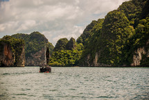 Boat sailing in the ocean water near tree covered mountains.