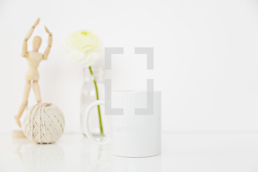 white flower in a clear vase, yarn, and wooden figurine 