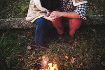 a couple sitting on a log next to a campfire 
