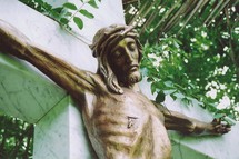 A bronze sculpture of Jesus on the cross made out of bronze hanging on a marble cross. Jesus is shown with a wound where a roman solider pierced his side with a spear. 