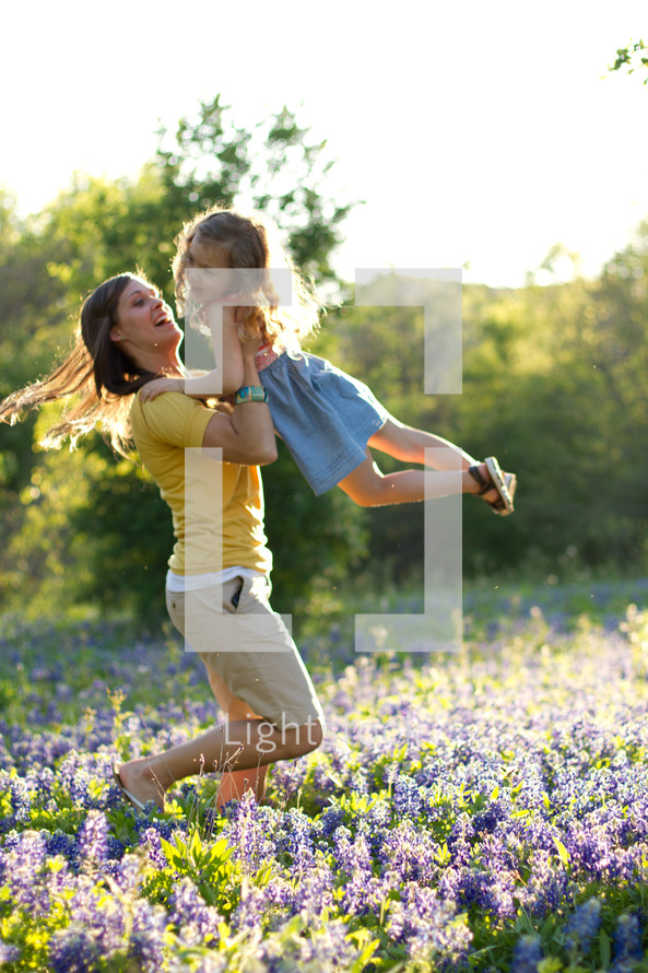mother holding and swinging her child in a field of blue bonnets