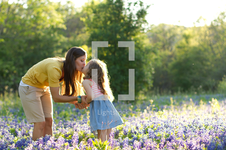 Mother and young daughter kissing in field of purple wildflowers