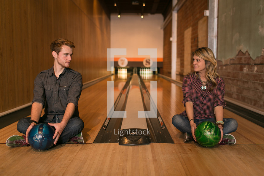 Couple sitting in bowling lanes with balls