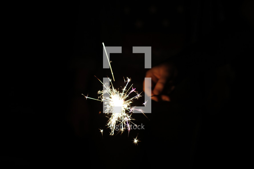A hand holding a lit sparkler in the dark.