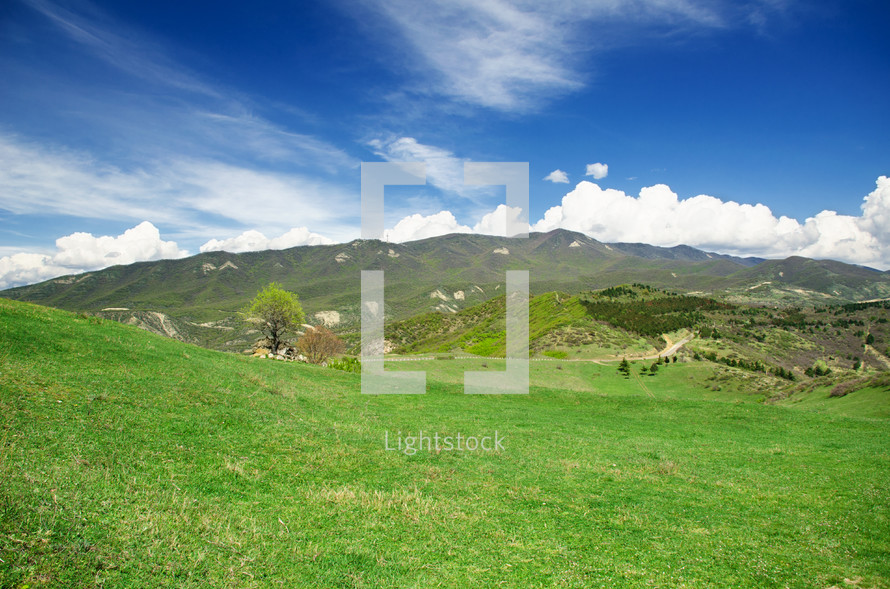 Green meadow and rolling hills in front of a mountain range.