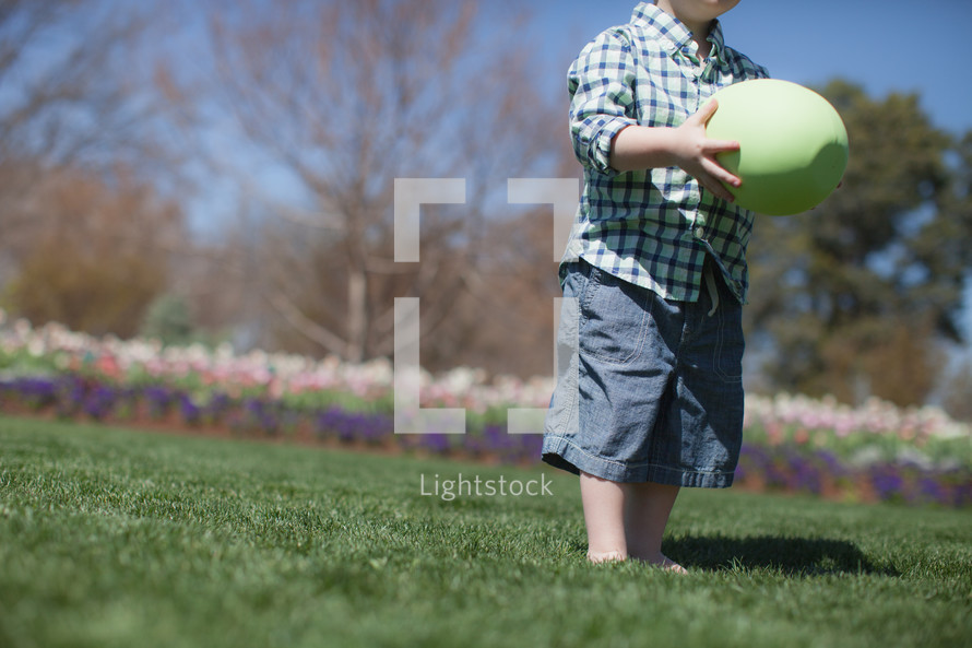 Young boy holding an oversized Easter egg, in a flower garden