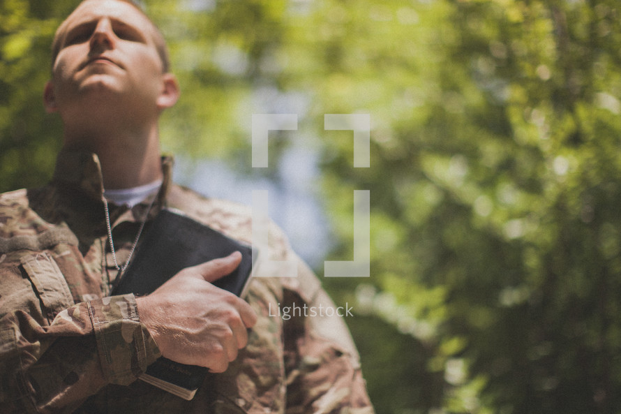 serviceman holding a Bible over his heart in prayer
