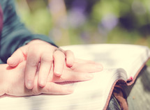 Hands folded on top of an open Bible.