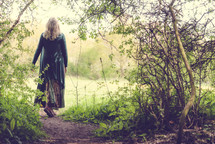 A woman walks along a path in the woods.