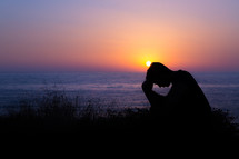 silhouette man with his head bowed in prayer at sunset 
