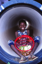 a girl child with a basket of vegetables in a tunnel 