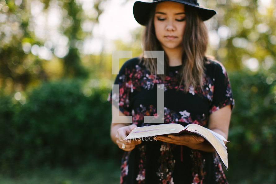 portrait of a young woman standing outdoors reading a Bible 
