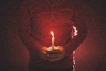 A man wearing a red shirt holding a candle