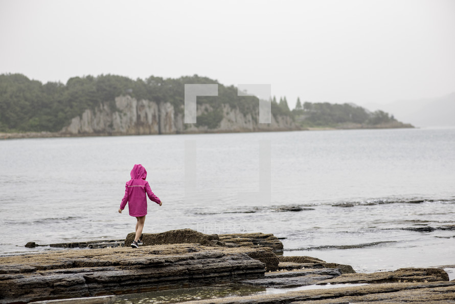 A little girl in a pink rain jacket walking on the coast line in Korea