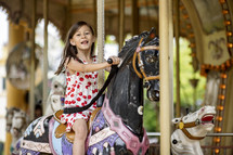 A young girl in a cherry dress riding on a carousel 