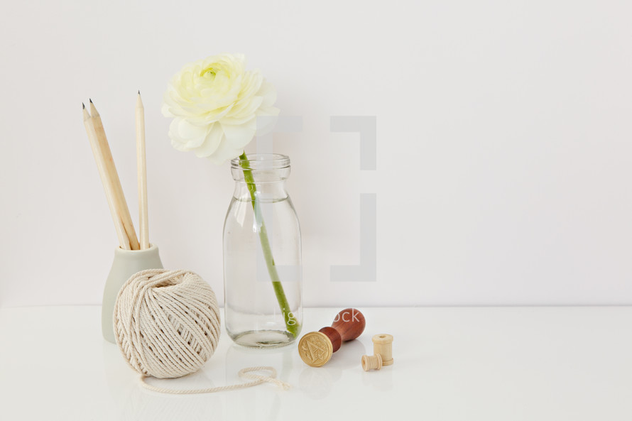 white flower in a clear vase, pencils, yarn, and stamp 